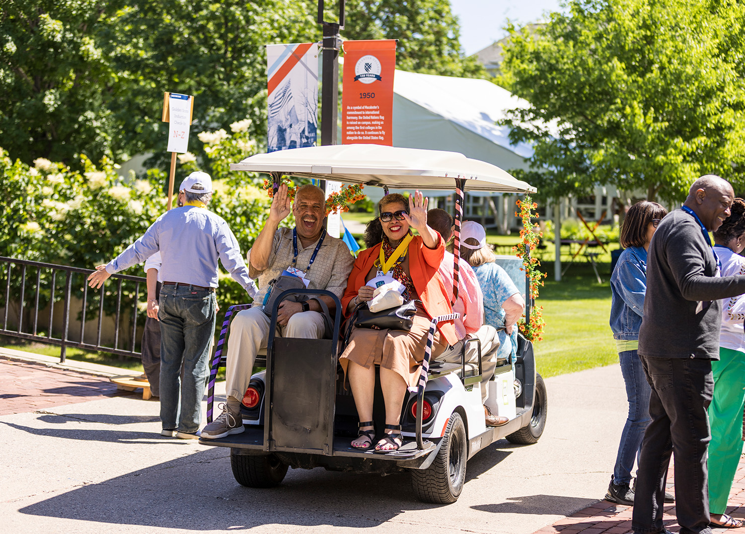 Two Reunion attendees wave as they ride on a golf cart