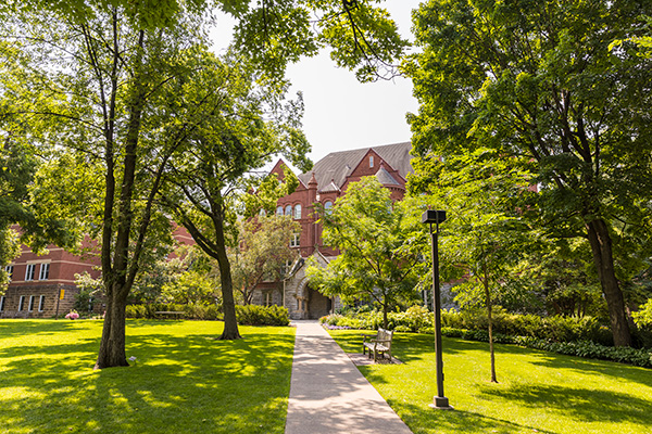 A sidewalk with green grass and green trees on either side, Old Main in the distance