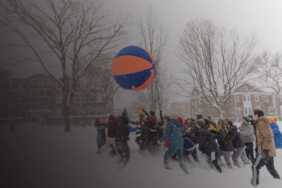 Macalester students hit a very large blue and orange ball into the air during a game of Pushball on a snowy day.