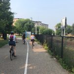 four students riding bicycles on a paved trail near railroad tracks