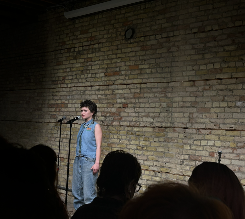 Adrien Wright '25 performs onstage in front of a brick wall in an all-denim outfit.