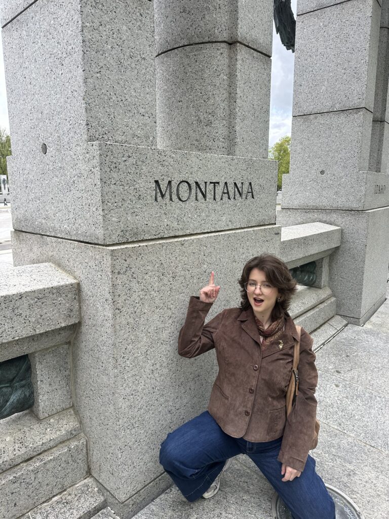 Chloë Moore squatting and pointing up to a part of a building that reads "MONTANA"