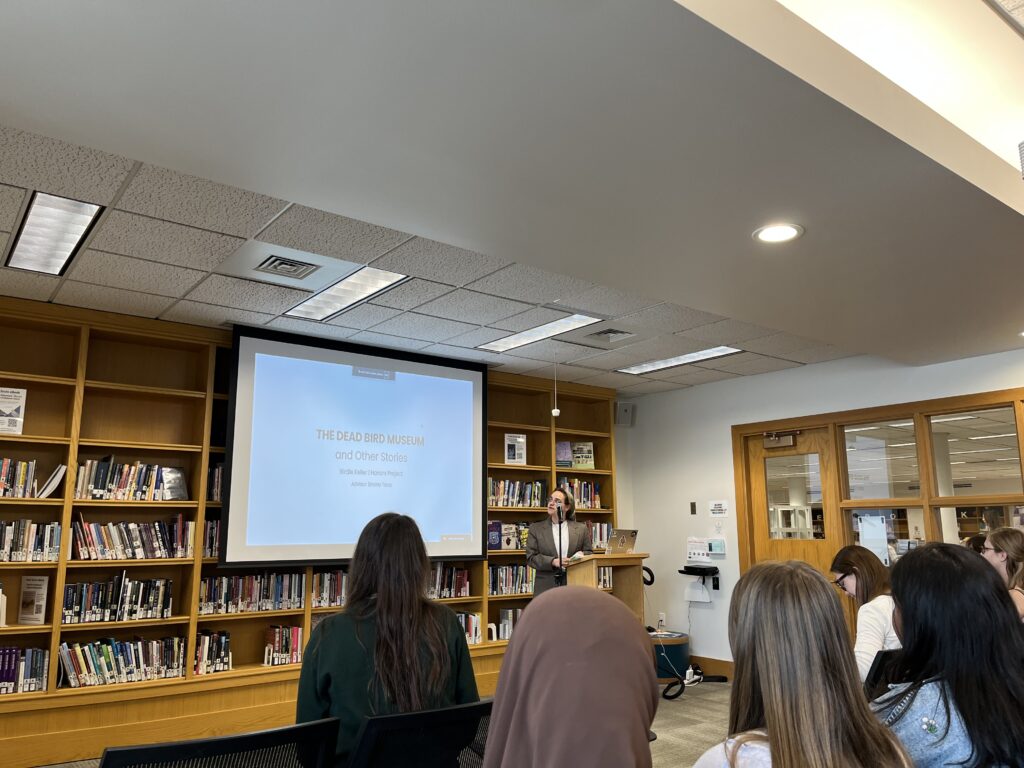 Birdie Keller presenting their Honors titled "The Dead Bird Museum" to a crowd of people 