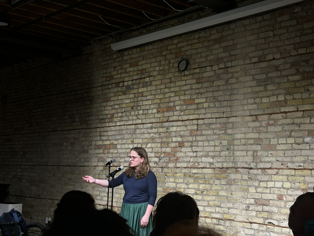 Veronica Kruschel '25 reaches out to the crowd in her performance in front of a pale brick wall at OpenBook.