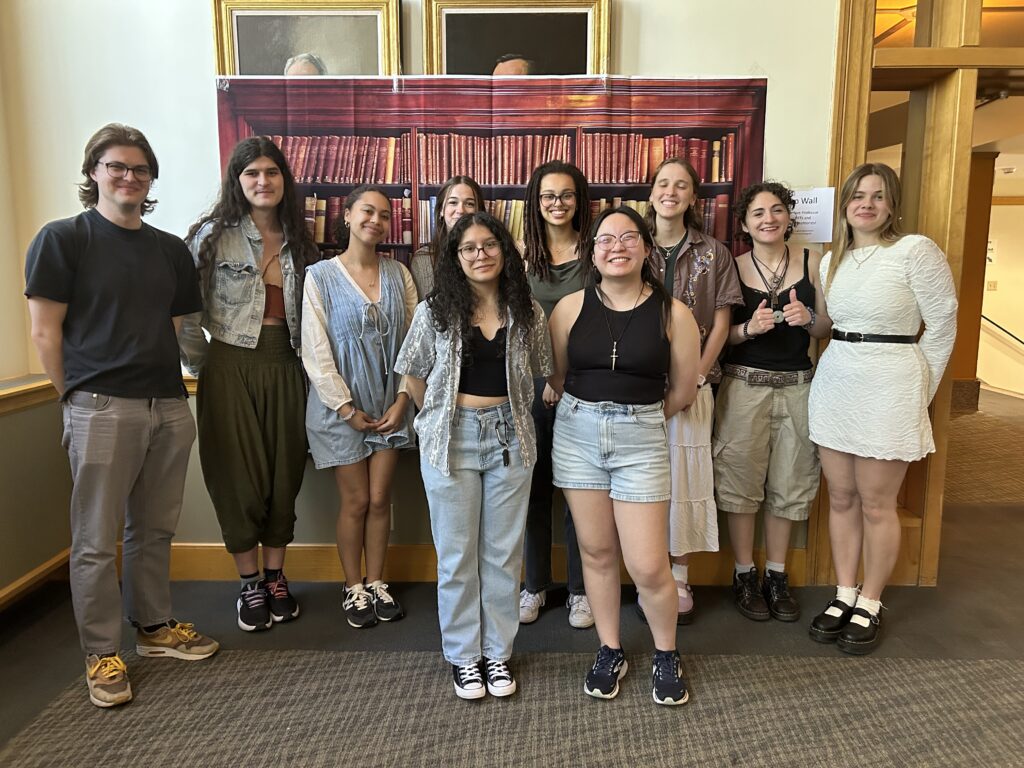 Many of the English Department student workers pose together in front of a background of books