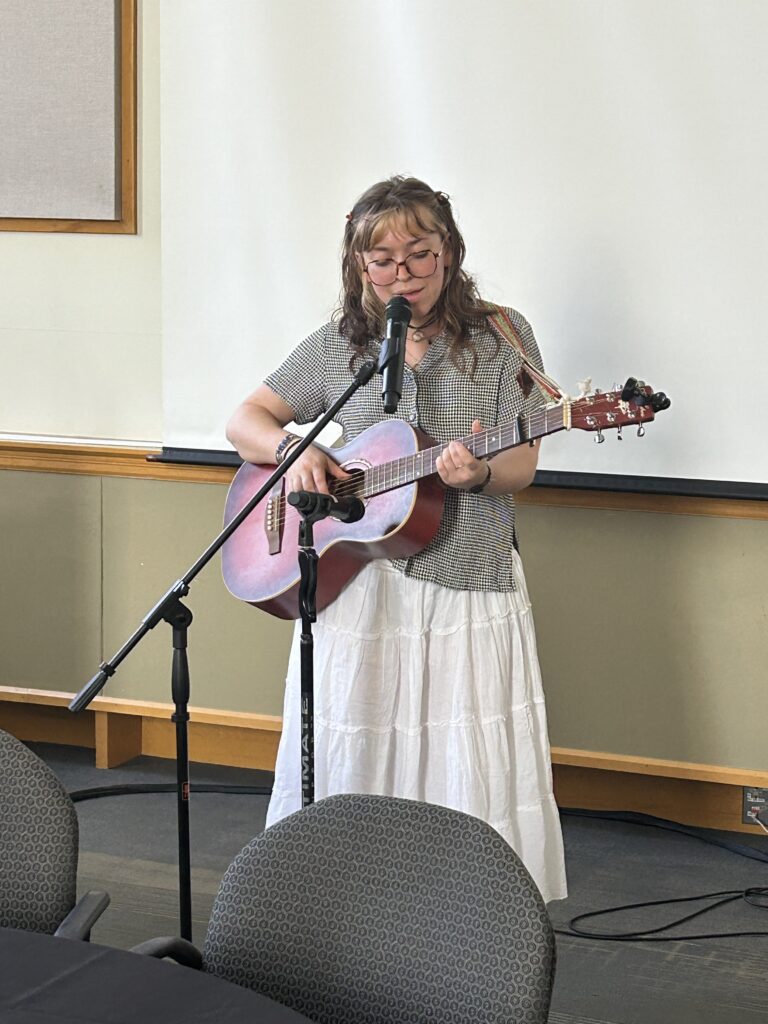 Eva Markim '25 serenades the crowd in the Weyerhaeuser Board room with pink guitar in hand.