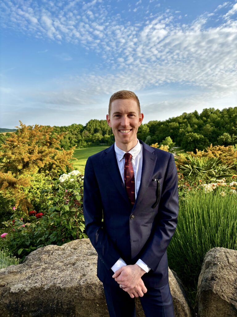 Adrian St. Francis '13 wears a suit in front of a backdrop of flowers and trees.