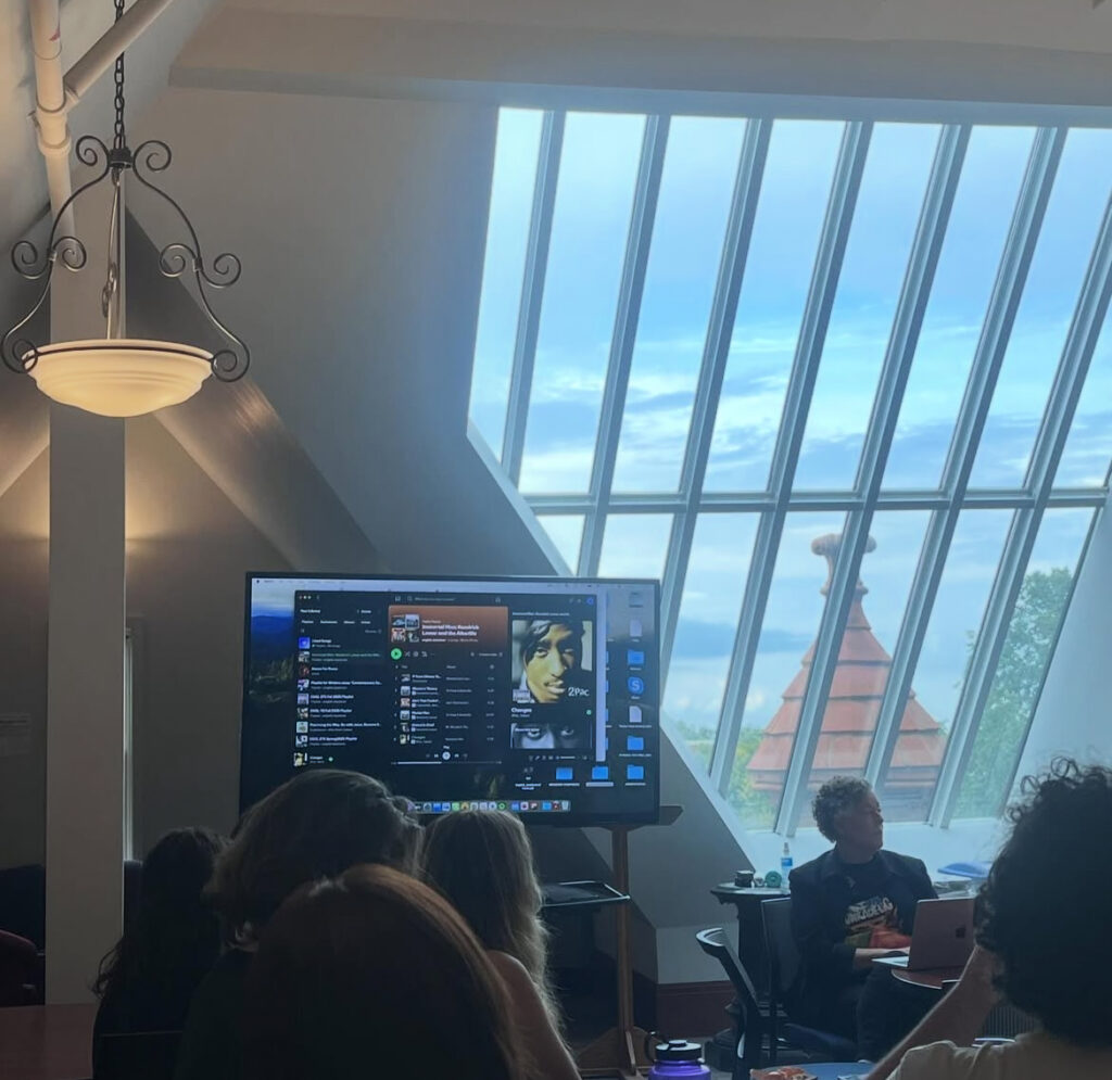 Prof. English presents at the Literary Salon with a clip from one of Tupac Shakur's songs playing in the background, displayed on the screen behind Prof. English.