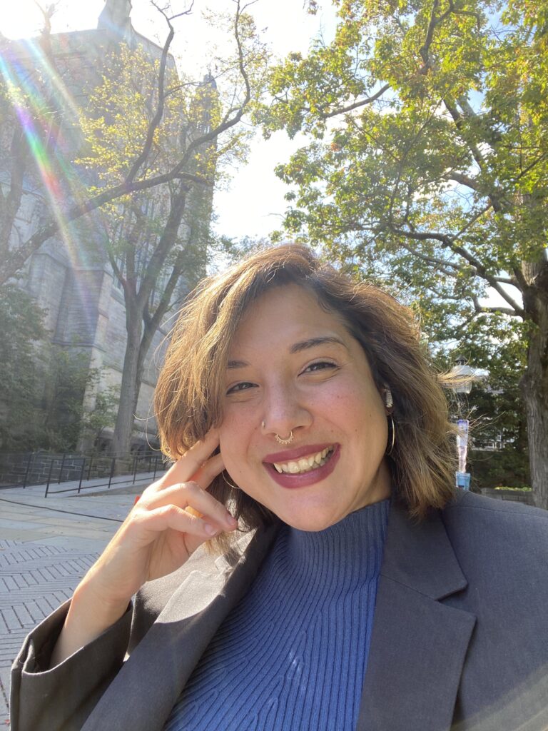 Coral Lumbley, posing outside in a blue turtle neck and blazer.