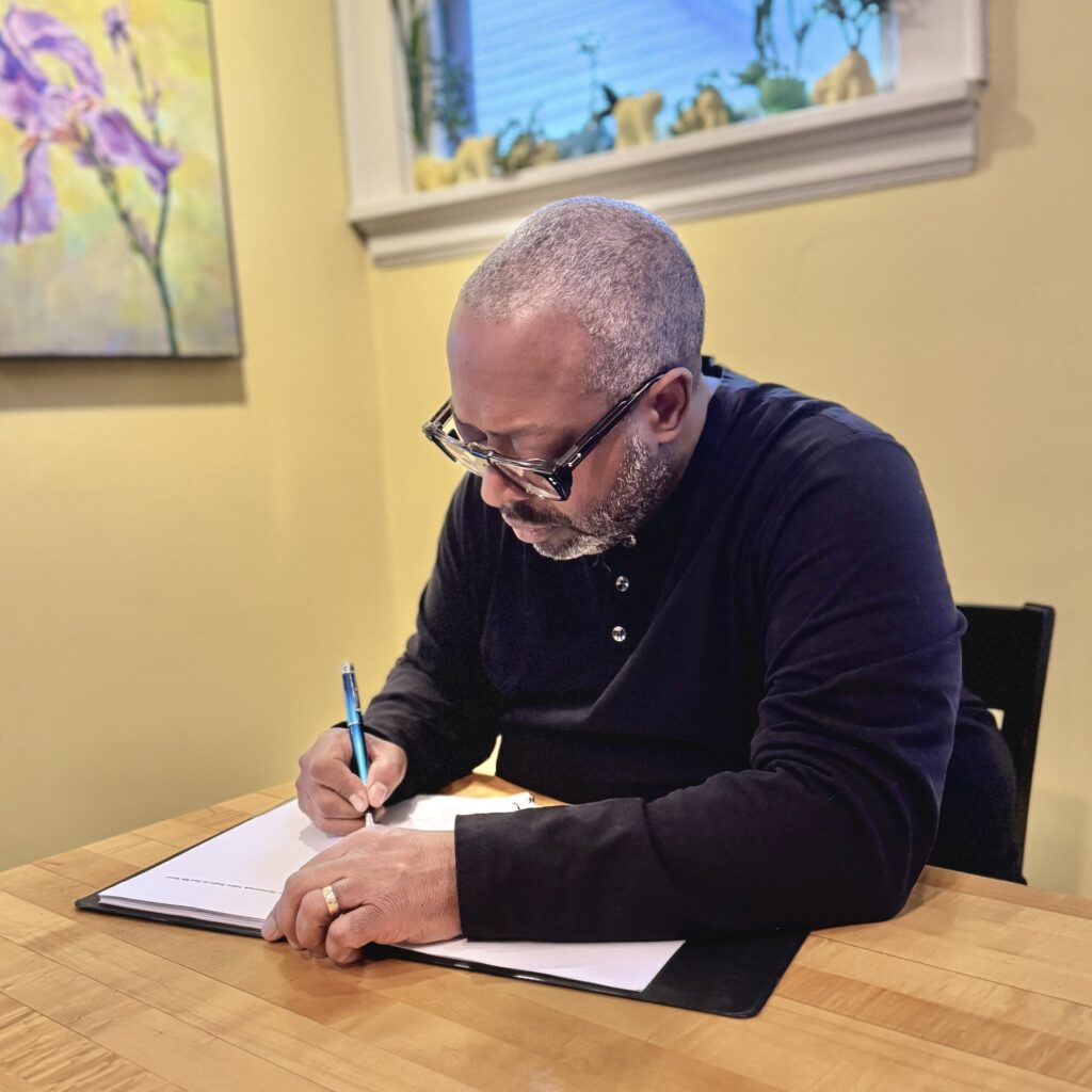 Photo of Michael Kleber-Diggs sitting down at a wooden table with a paper and pen in hand.