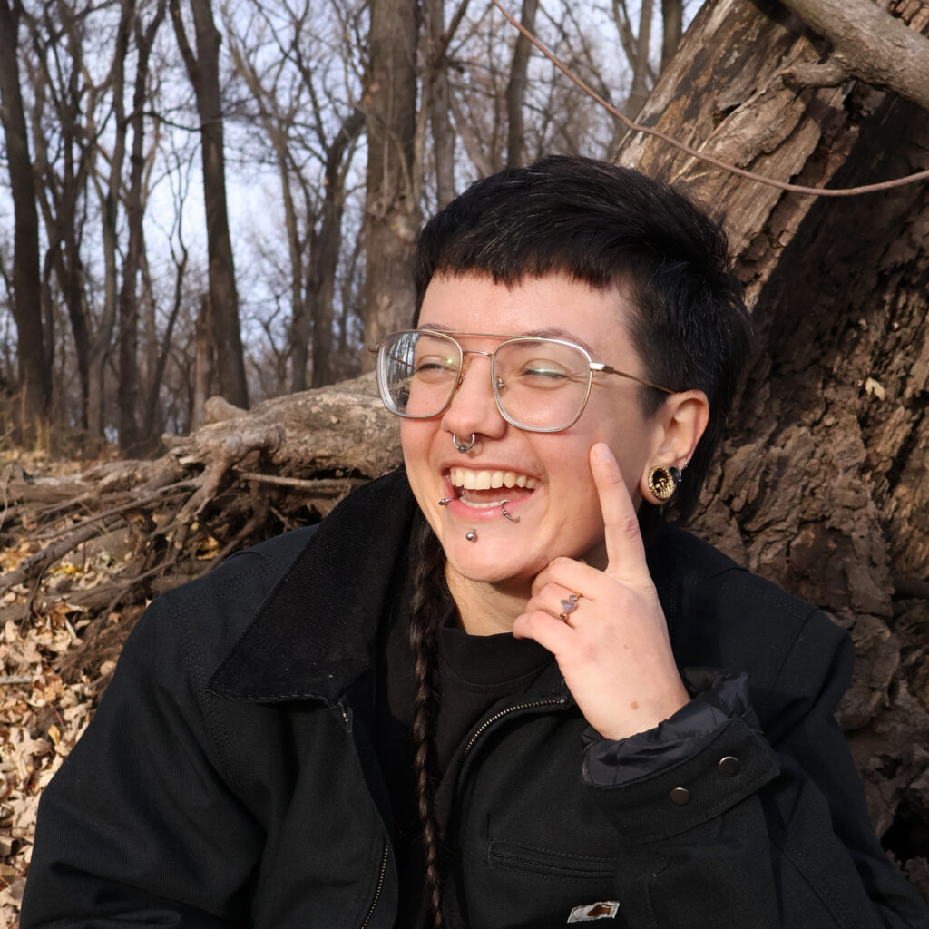 Photo of Ollie Schminkey '16 laughing in the woods, sitting up against a tree.