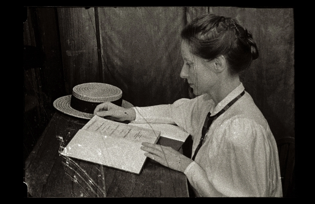 A black and white photo of a woman reading a book at the desk, taken from the Acts of Memory film.