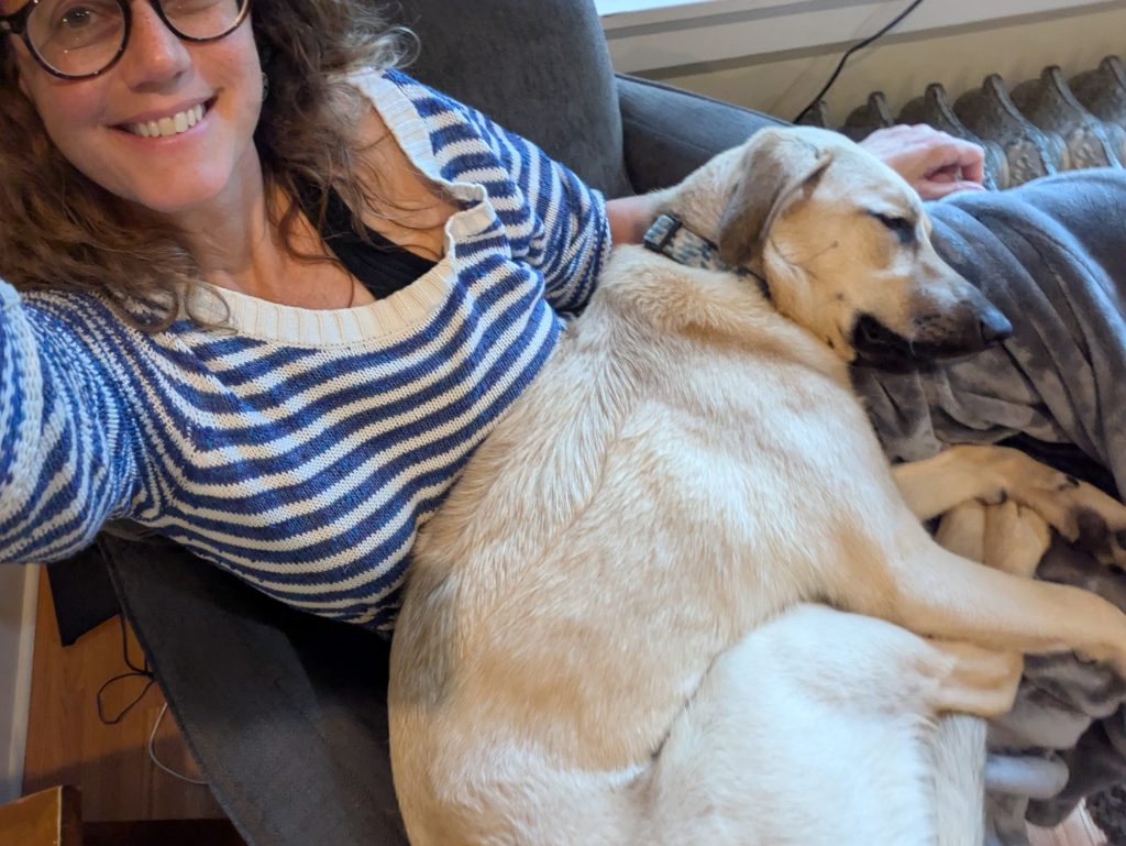 Andrea poses with her puppy, who is sprawled across her lap, fast asleep.