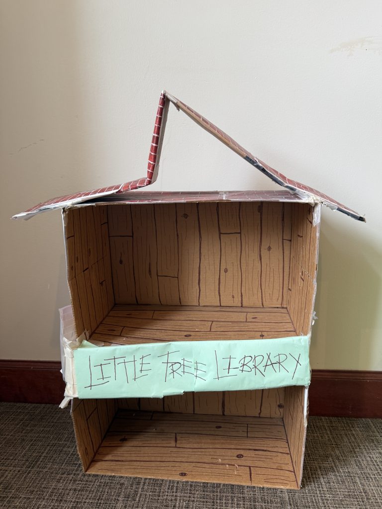 First version of the little library. Two shelves built out of cardboard with a handwritten sign in all caps saying "Little Free Library."