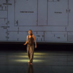 Dancer stands in front of a projection of a floor plan