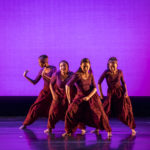 Dancers wearing red lean forward on stage
