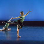 One dancer poses on the floor as a standing dancer lifts a leg behind them