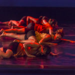 Several dancers lie pushing against the ground