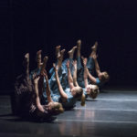 Dancers lying on the ground lift their arms and legs into the air