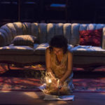 Actor kneels and lights a candle on stage