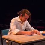Actor sits writing at a desk
