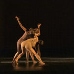Dancers in nude costumes crouch on stage together