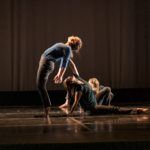 A seated dancer supports another as they lean backwards