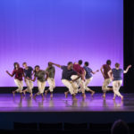 Dancers wearing white pants perform on stage