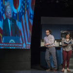Two actors perform on stage in front of screen showing news clip of Donald Trump
