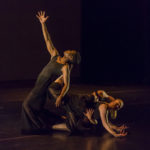 Two dancers lie tangled on the floor while a third reaches upward