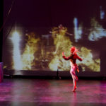 Performer spins in front of a projection of fire