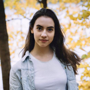 Student standing in front of a tree in autumn looks into the camera