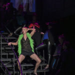 Actor wearing a bright green boa dances on a staircase