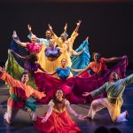 Dancers in colorful costumes pose with their arms outstretched