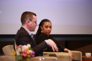 Two speakers sit in chairs on stage