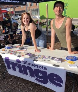Elinor and a coworker standing by a table advertising Minnesota Fringe Festival
