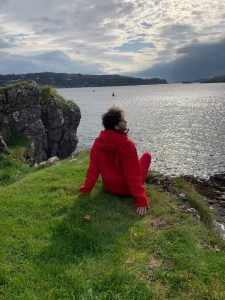 Adam sitting on a grassy cliff overlooking the water