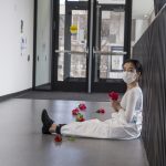 Performer sits in hallway surrounded by red flowers