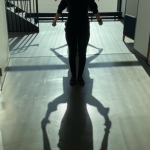 Performer stands in a hallway with dancing shadows