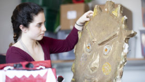 Mina holding a large clay mask