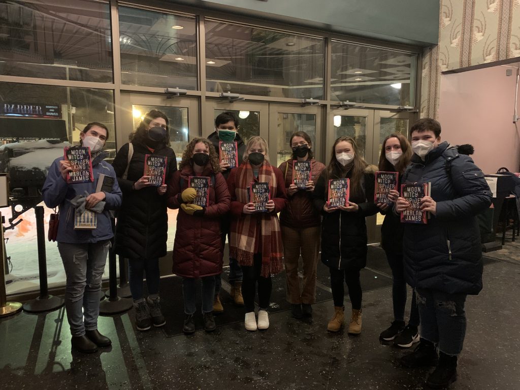 Nine students hold their signed copies of Professor James's new book, Moon Witch, Spider King, in front of the entrance to the Parkway Theater.
