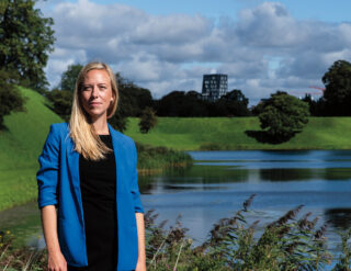 Nina Porst standing in a park in Denmark. A pond and several trees are visible behind her.