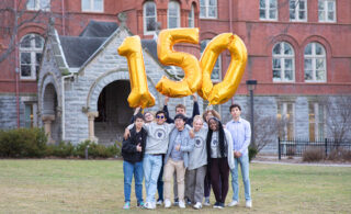 A group of nine Macalester students hold gold 150 balloons