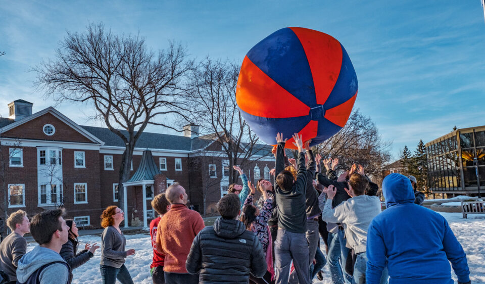 Students reach for a giant blue and orange ball in a game of push ball on the Great Lawn.