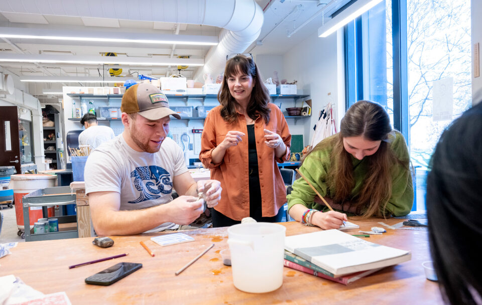 Two students in a class about Chinese art hold brushes as they talk with their professor.