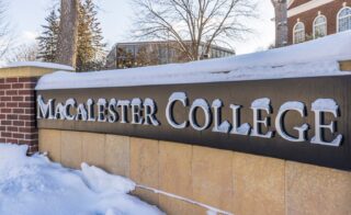 A Macalester College sign bears raised letters that are covered in a few inches of snow.