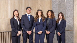 Five students dressed in business attire pose for a photo