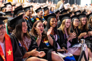 A group of students in caps and gowns sits and claps at Commencement 2025