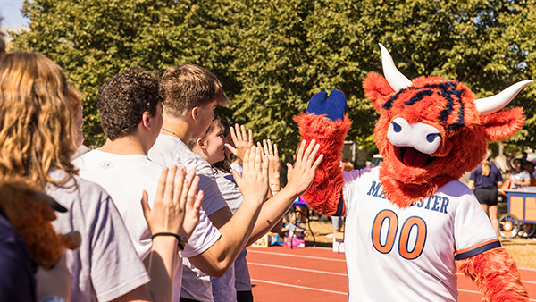 Students high five Coo, Macalester's orange highland cow mascot