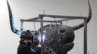 A sculptor works on the metal head of Macalester's new Coo sculpture.